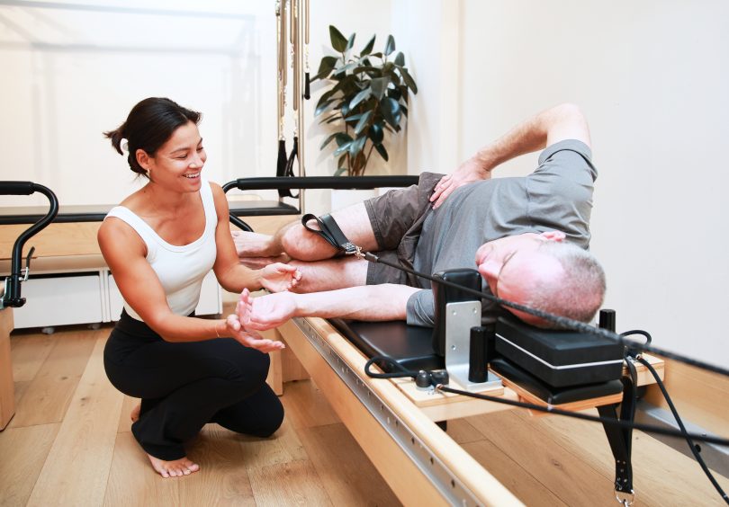 Physiotherapist assisting male patient with side-lying Clinical Pilates reformer exercise at Malvern Physiotherapy Clinic.