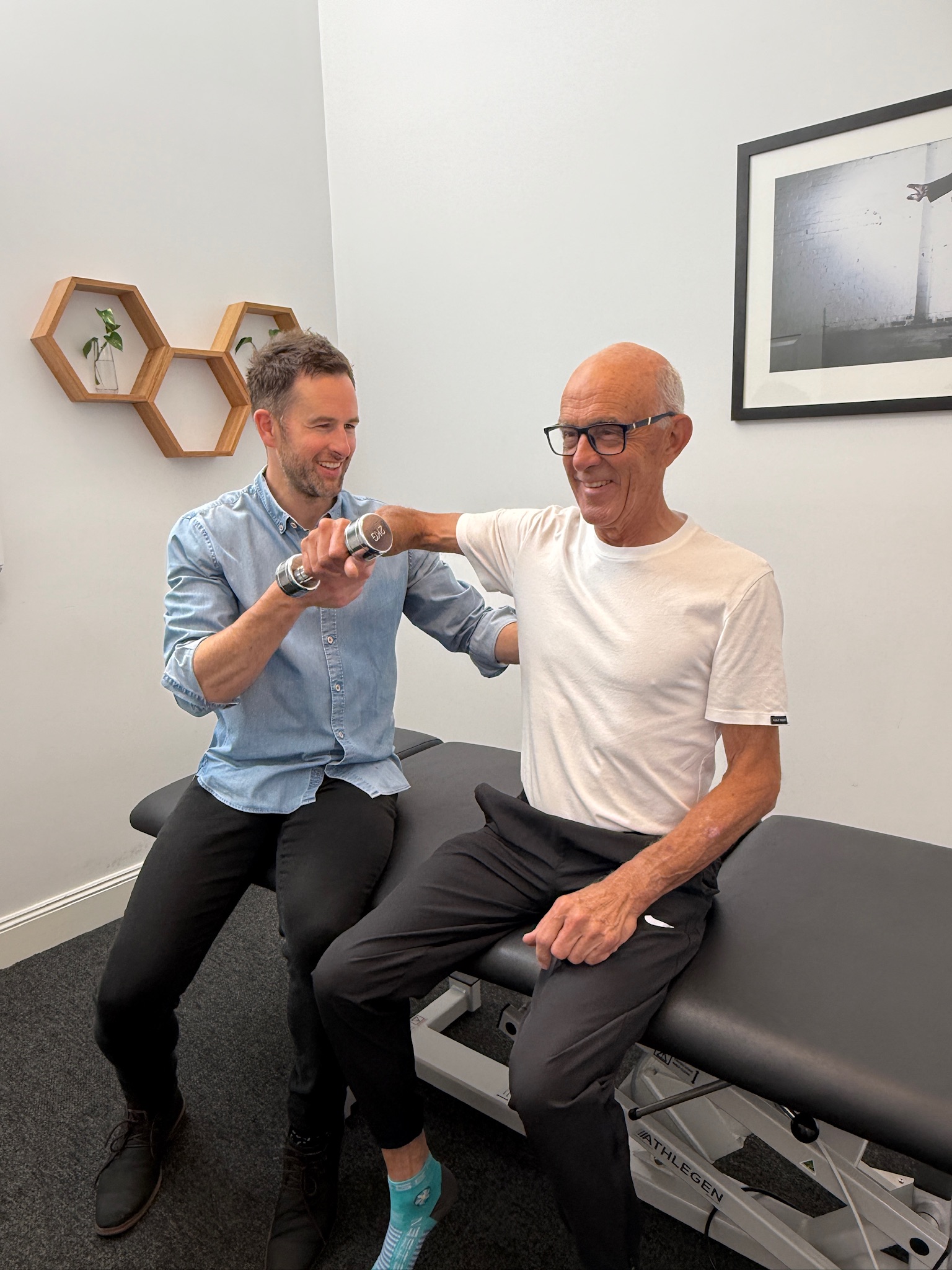 Senior man completing a shoulder strengthening exercise with physiotherapist guidance