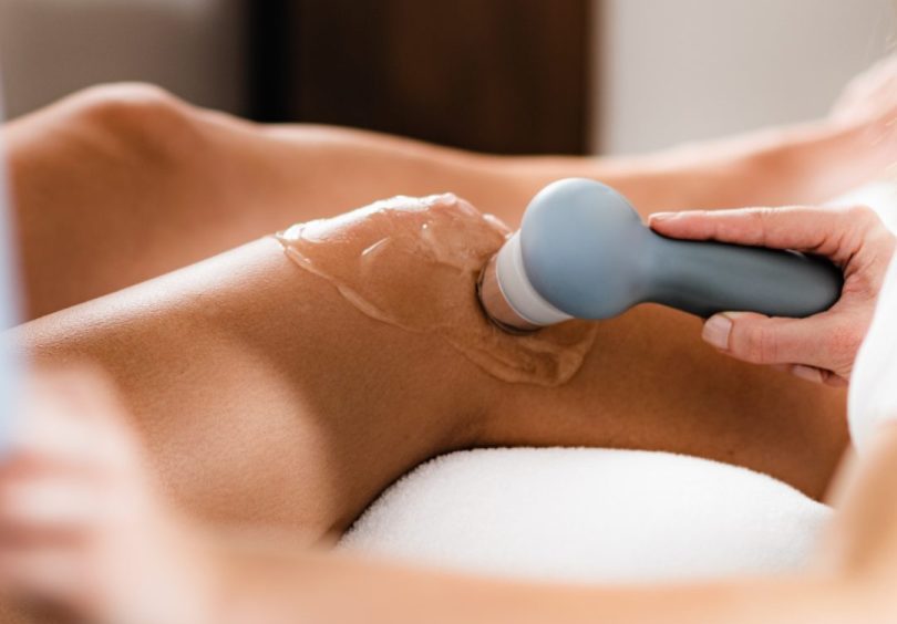 Physiotherapist using real-time ultrasound device to assess muscle activation on a patient’s lower back with ultrasound gel applied.