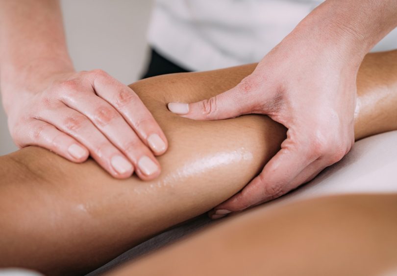 Remedial massage therapist applying soft tissue treatment to a patient's calf muscle to help reduce tension, stiffness and muscle discomfort.